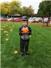 A child in a dinosaur costume, holding a pumpkin