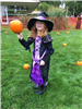 A child dressed as a witch, holding a pumpkin