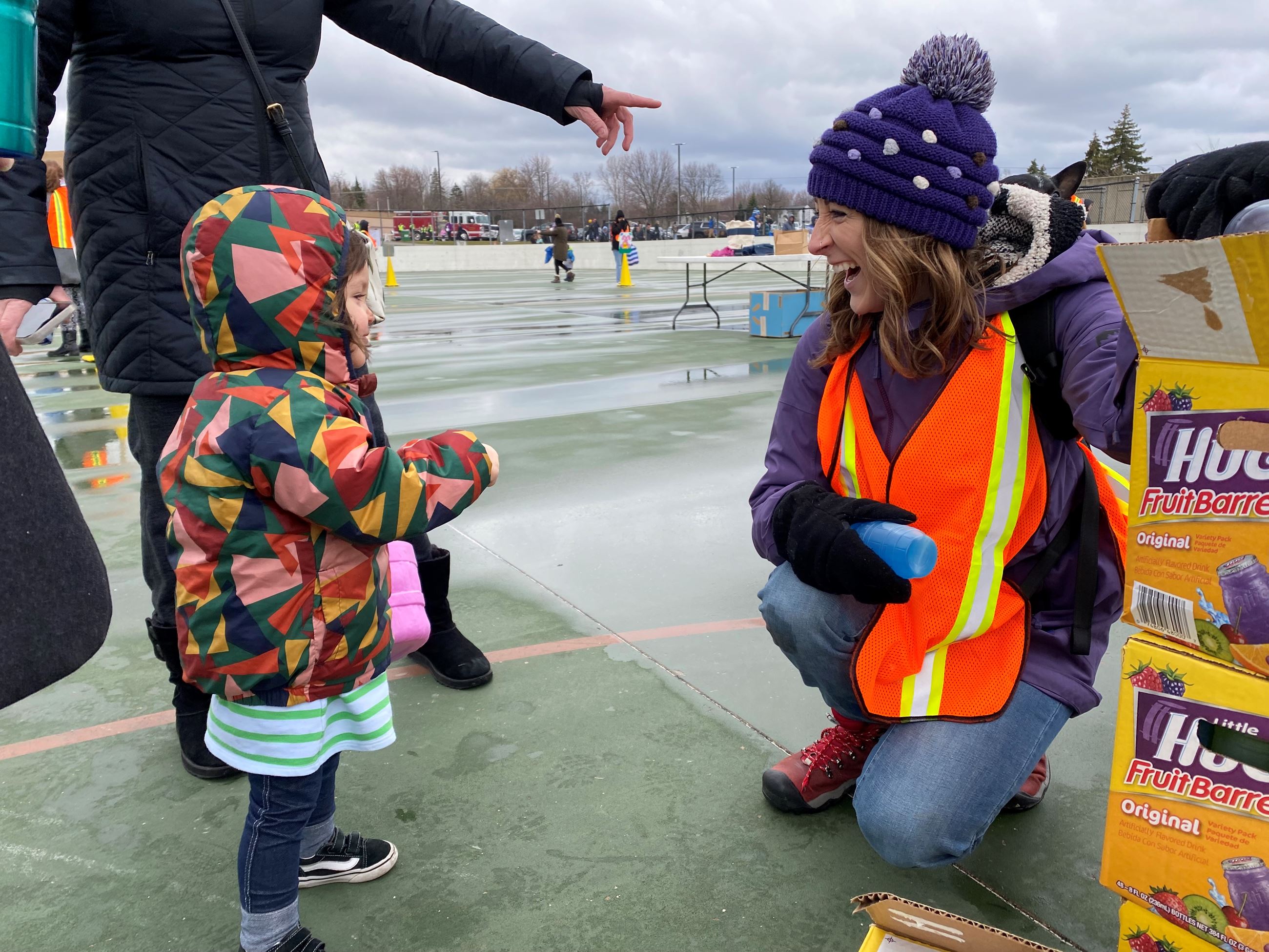 Child wearing multi-colored jacket at easter egg hunt talking with a volunteer