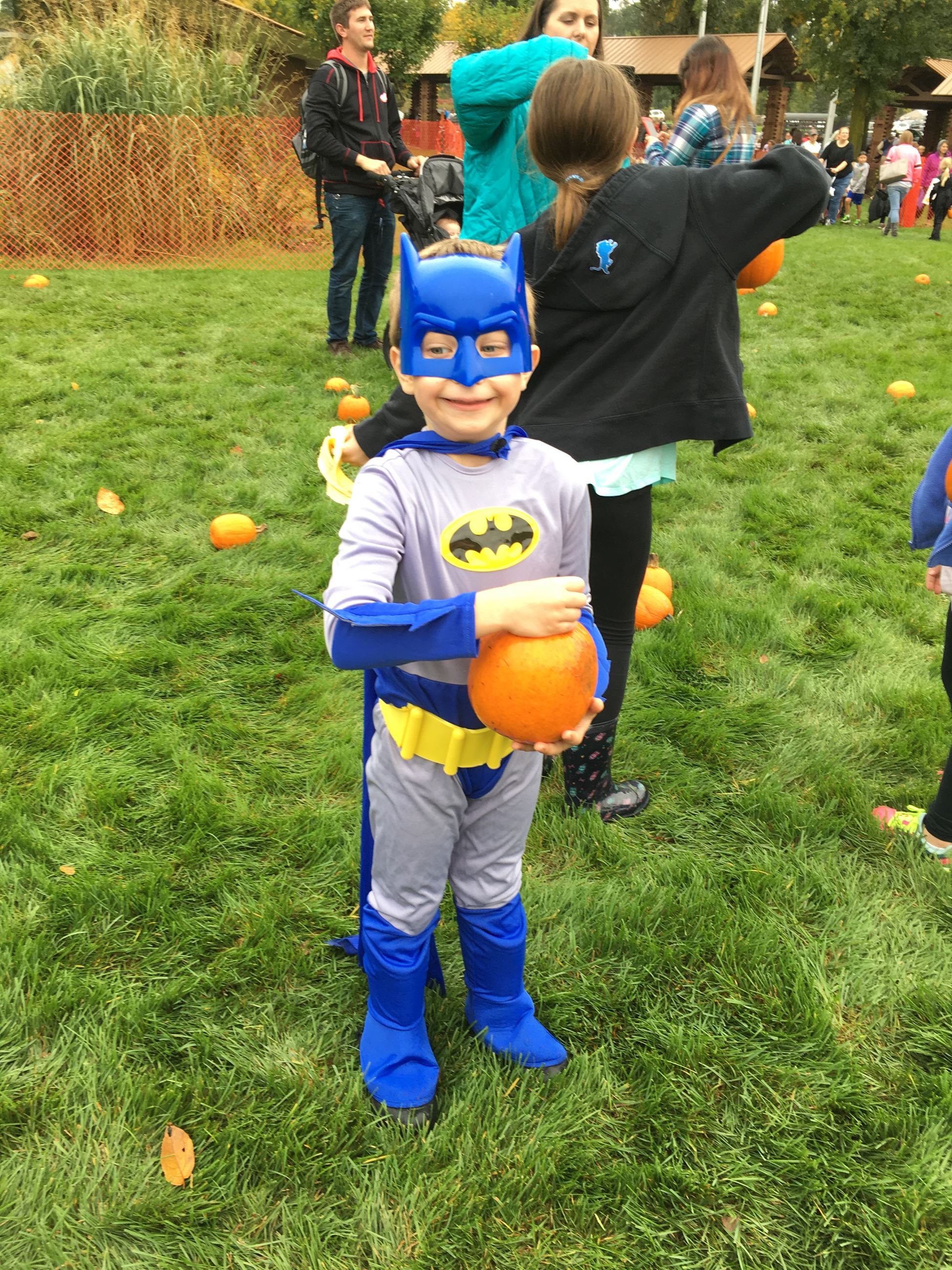 A child in a Batman costume, holding a pumpkin