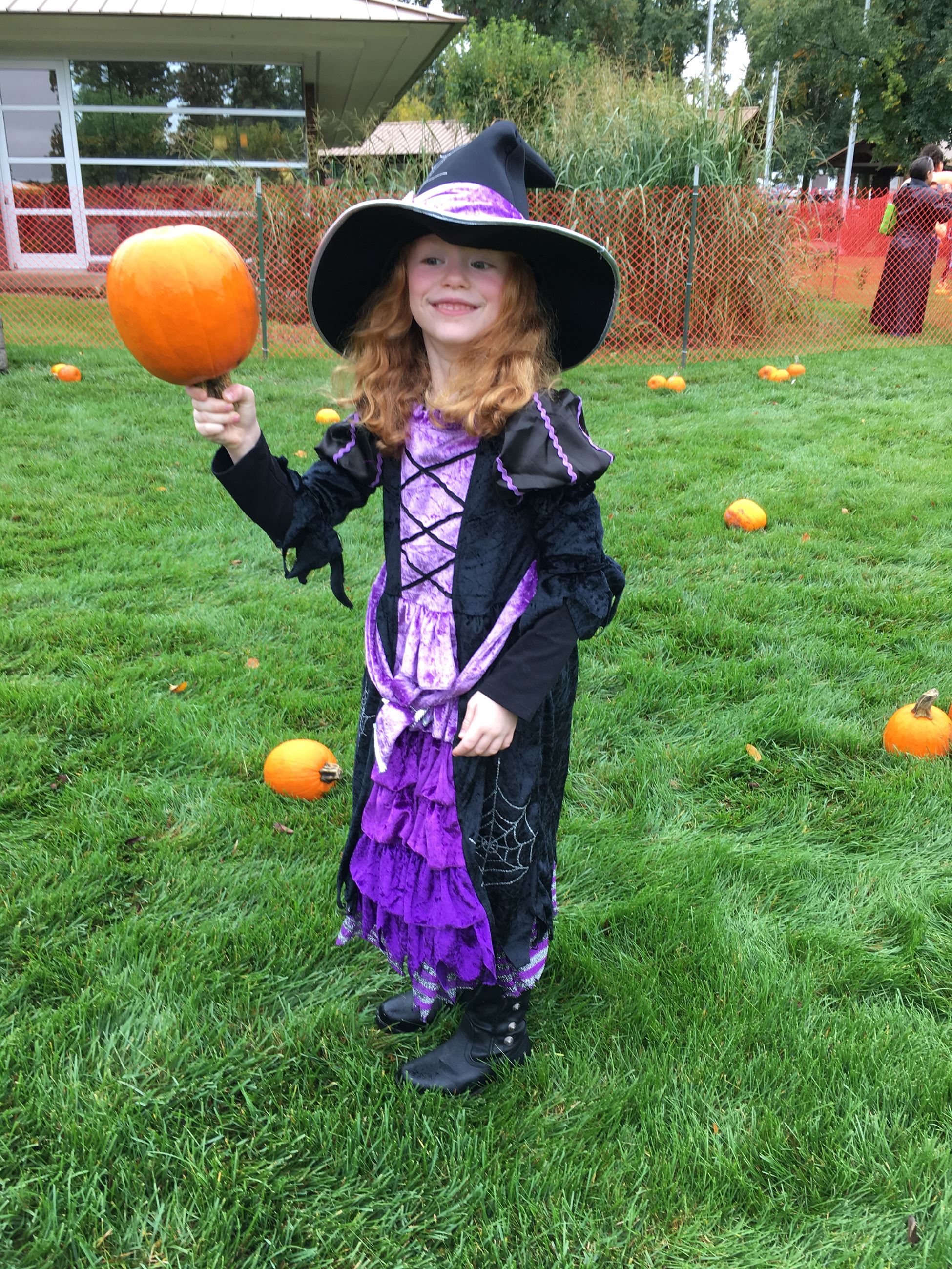 A child dressed as a witch, holding a pumpkin